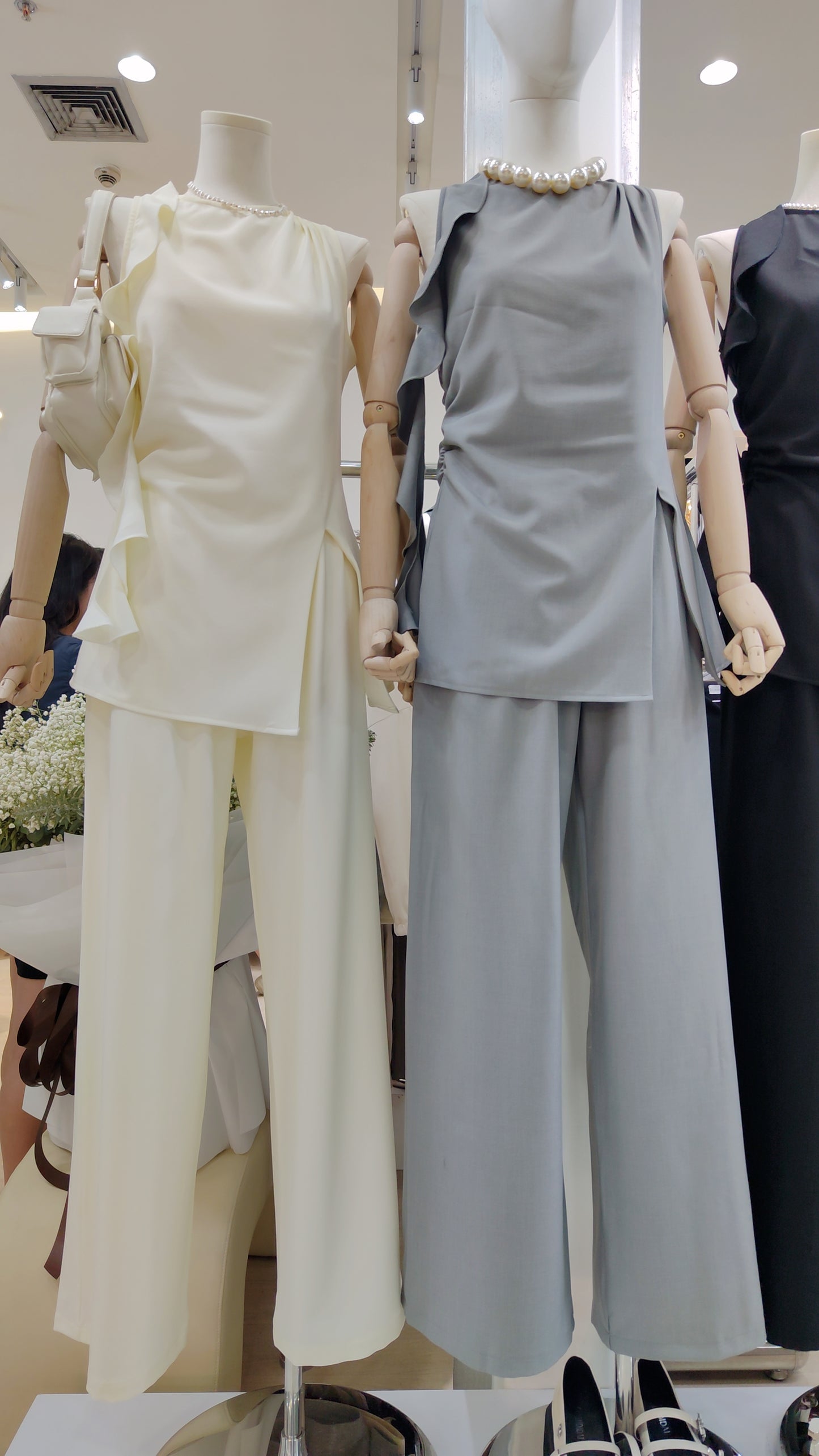 The "Flowy Tunic" Two-Piece Set in cream and gray with sleeveless ruffle hem tops and wide-leg pants displayed on mannequins.
