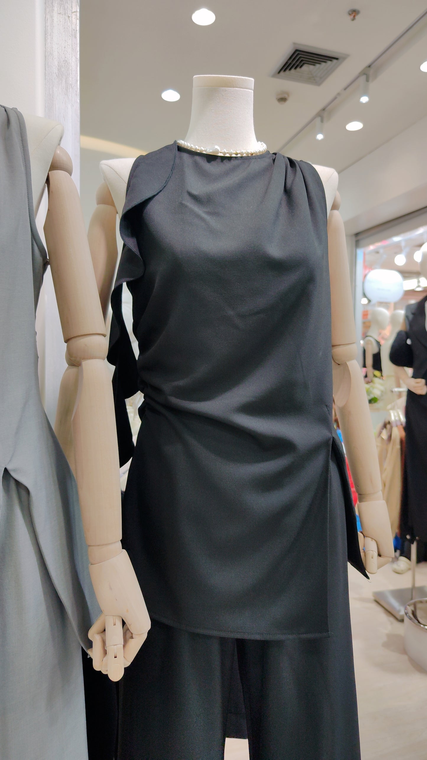 The "Flowy Tunic" Two-Piece Set in black with sleeveless ruffle hem tunic and wide-leg pants on mannequin.