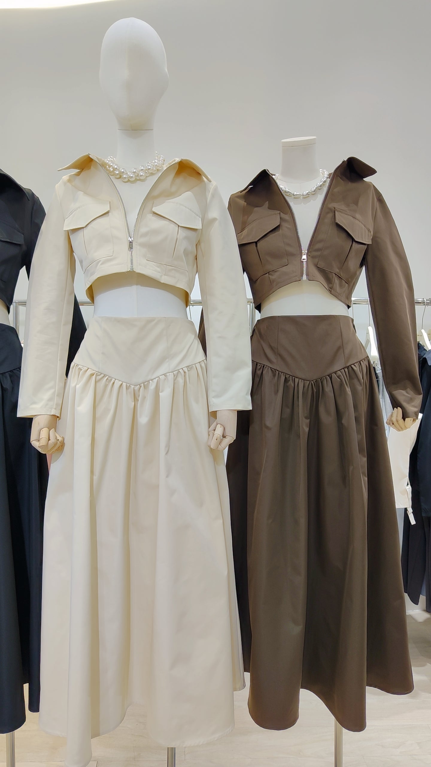 Two mannequins wear the Classic Vest Co-ord Set in cream and brown featuring a zip-front vest and long skirt.