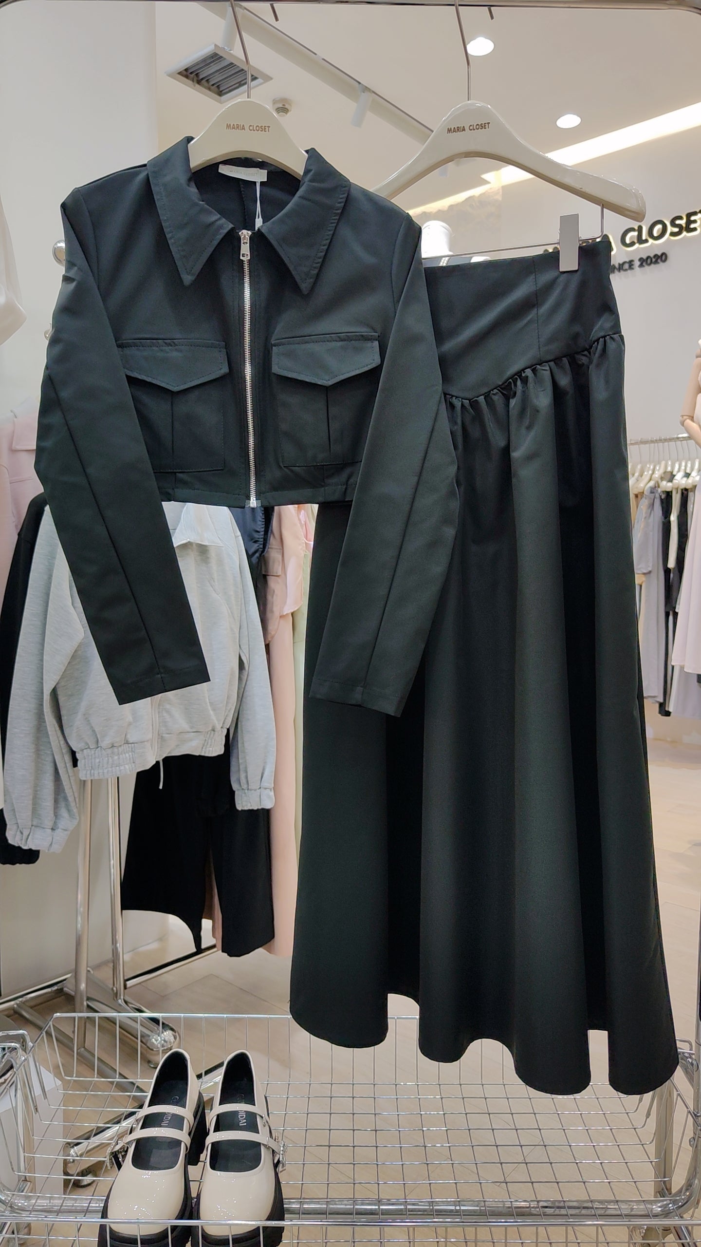 The "Classic Vest" Co-ord Set in black with a zip-front vest and matching long skirt on hangers in a boutique.