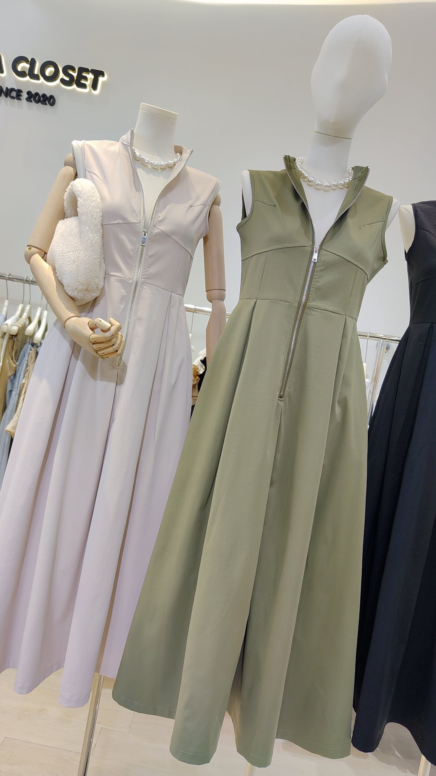 Two mannequins dressed in cream and olive Urban Zip-Front Maxi Dress with sleeveless design and front zipper detail.