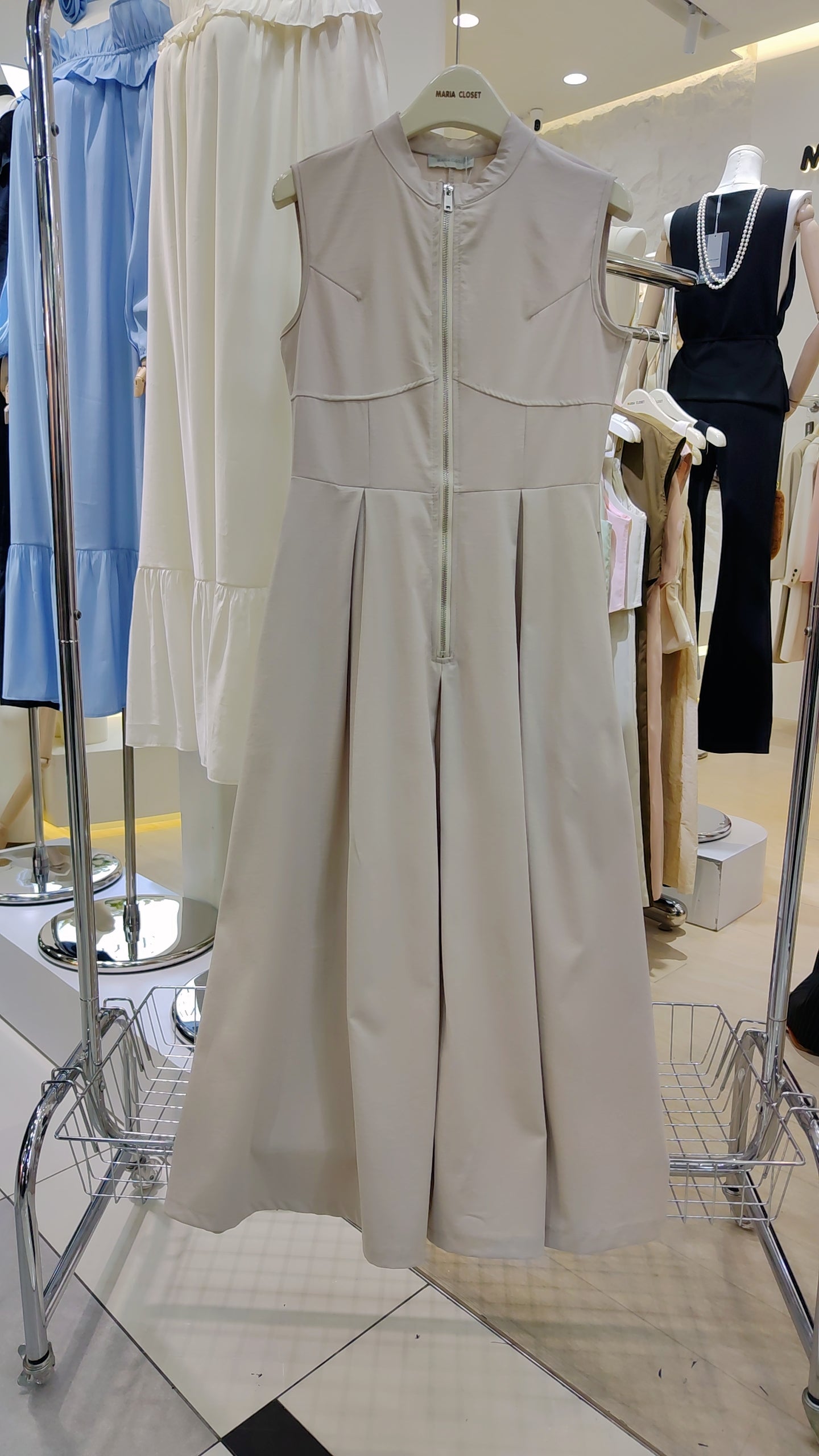 The "Urban Zip-Front" Maxi Dress in beige with sleeveless design and full front zipper on display in store.