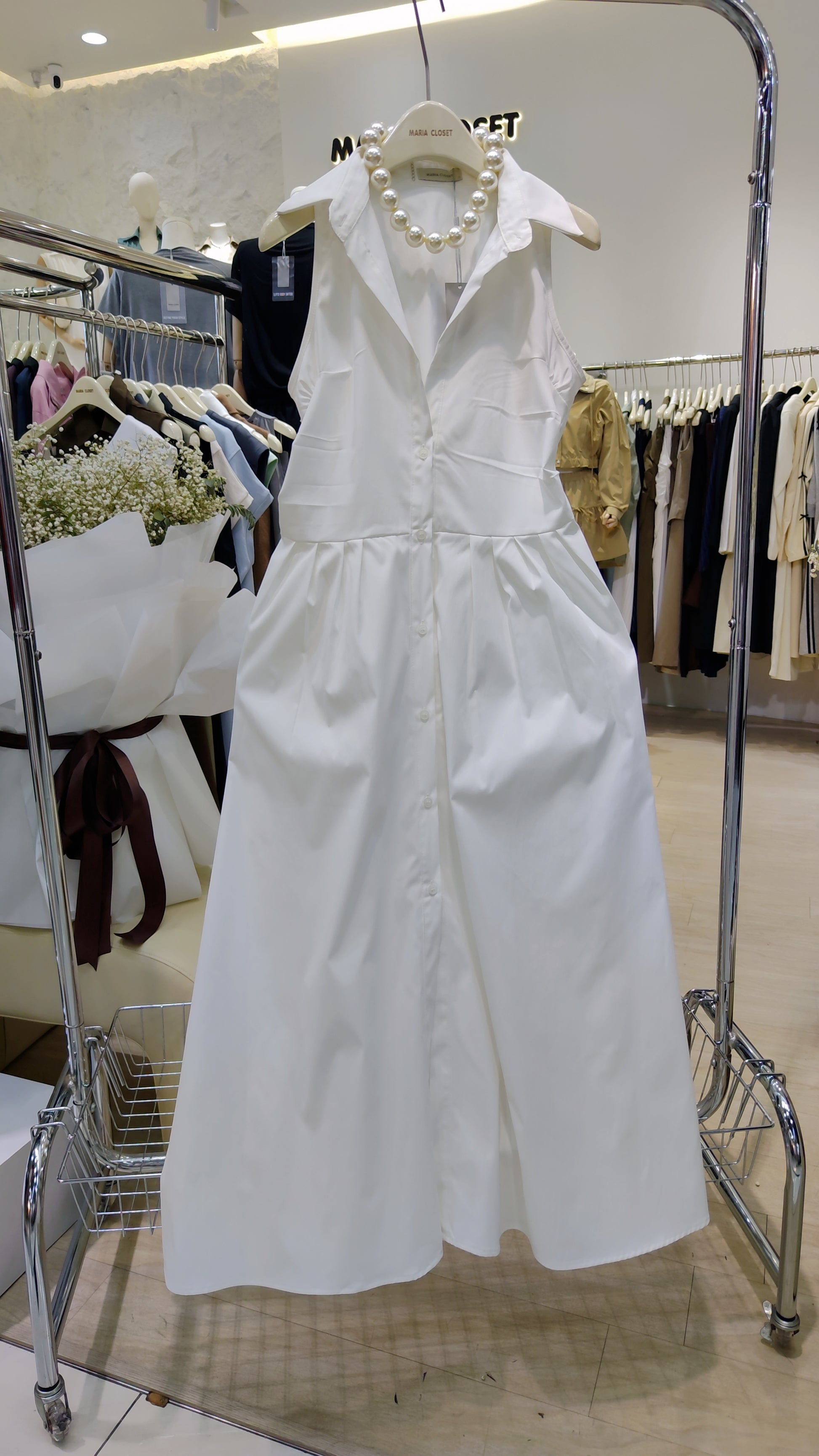 The "Everyday" Sleeveless Shirt Dress in white cotton with button-front and classic collar, hanging in a boutique.