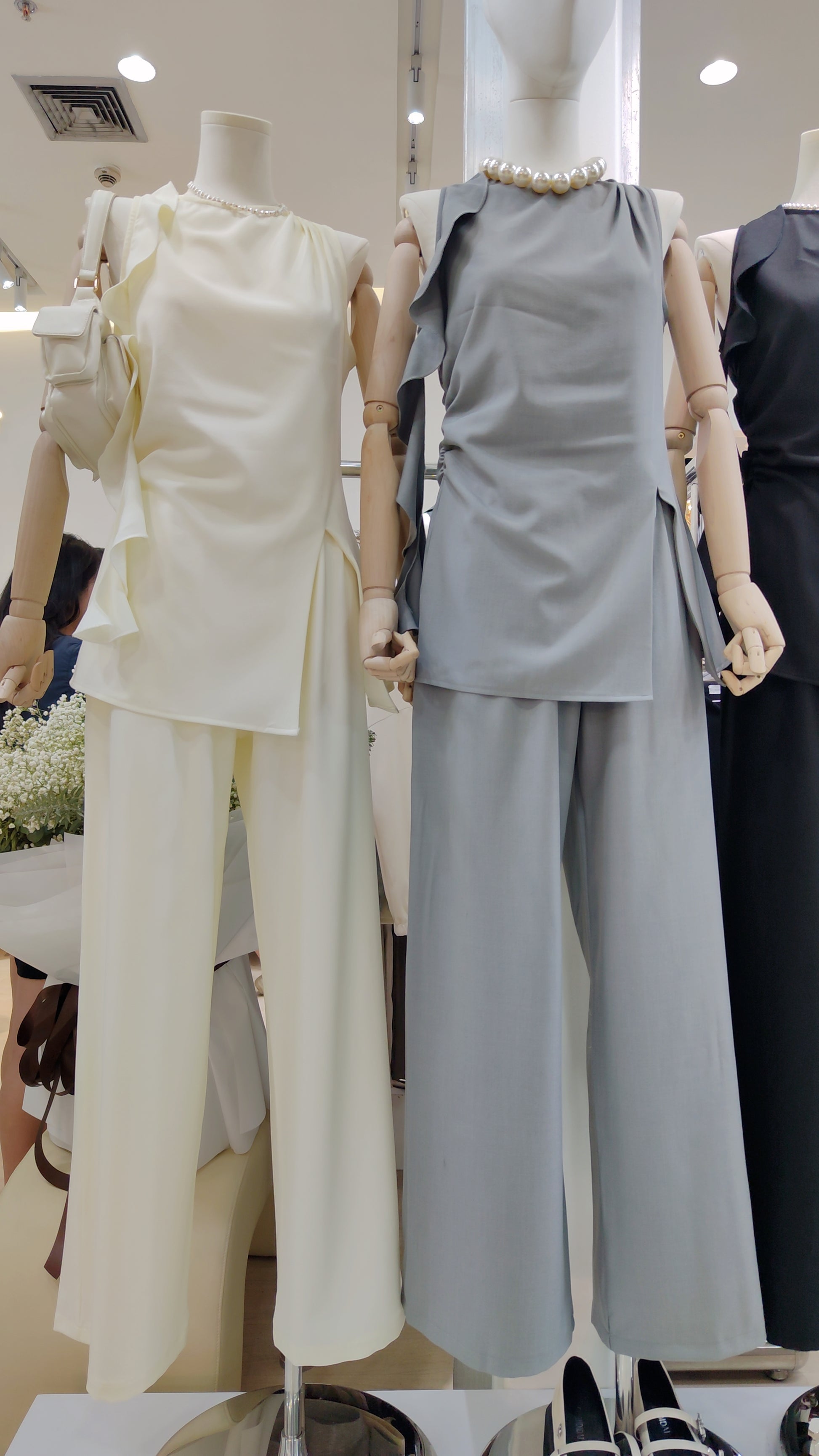 The "Flowy Tunic" Two-Piece Set in cream and gray with sleeveless ruffle hem tops and wide-leg pants displayed on mannequins.